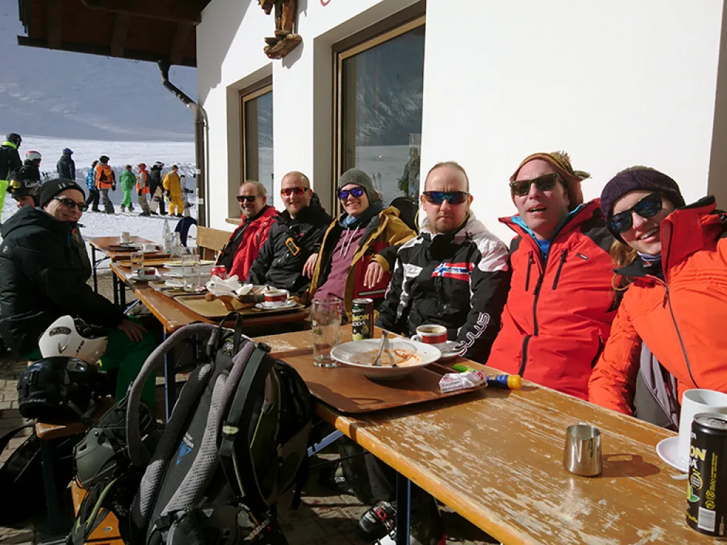 Erwachsene sitzen an einem Tisch vor der Hütte.